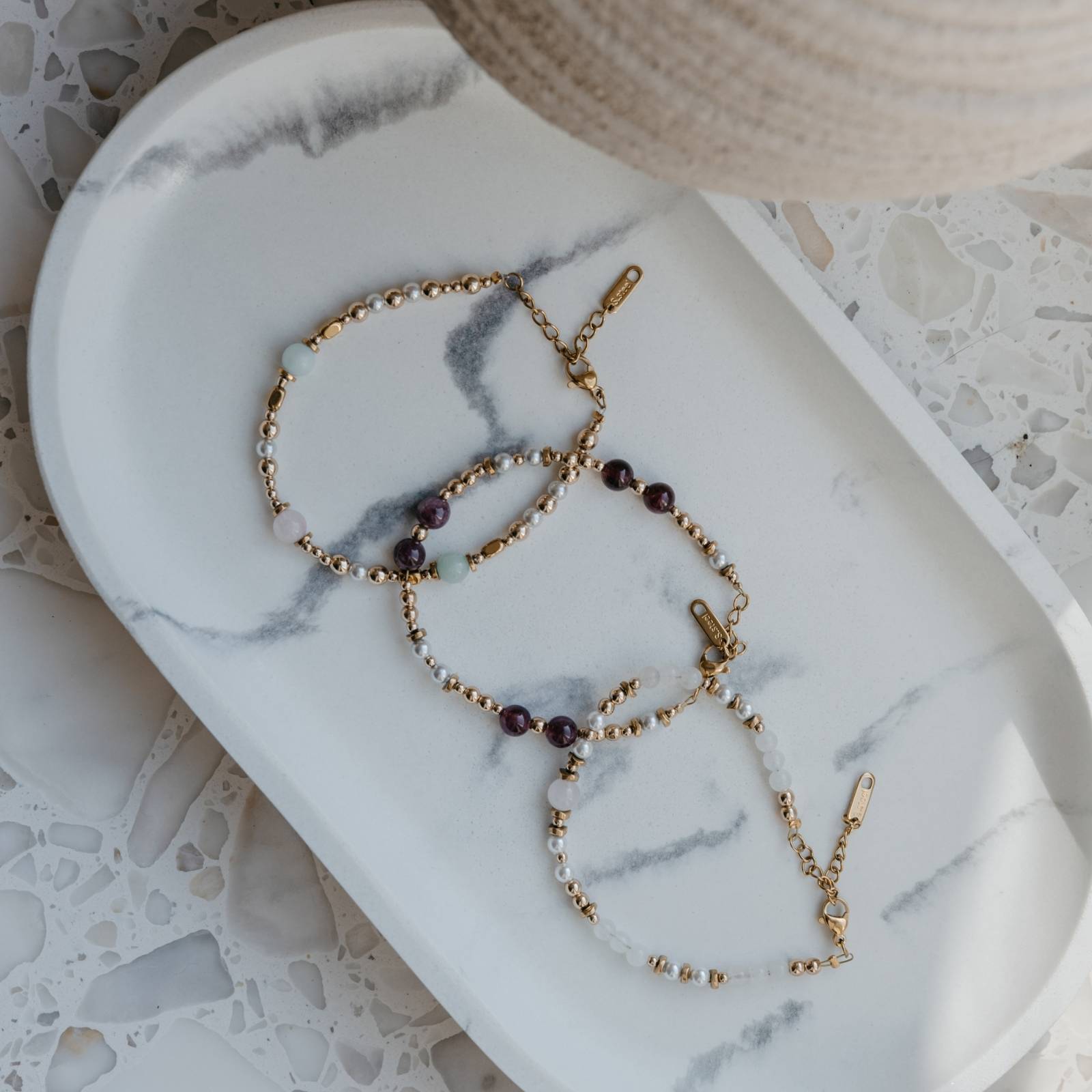 Bransoletka z granatu, pereł i hematytu w zestawie z innymi bransoletkami z kamieni naturalnych na marmurowym talerzu – kolekcja premium