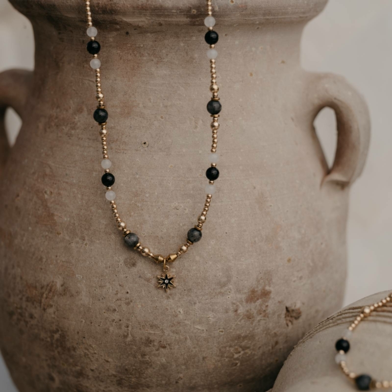 Naszyjnik z labradorytu, hematytu, czarnego agatu i białego jaspisu z zawieszką w kształcie gwiazdy na tle glinianego dzbana — elegancka biżuteria naturalna